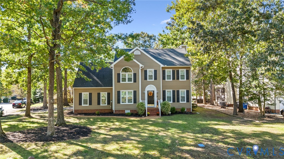 Two-story residence featuring tan lap siding, a dark-toned shingled roof, arched accent window, brick foundation skirting, and shuttered windows
