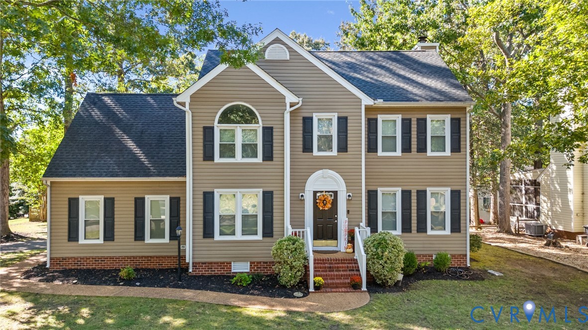 Two-story colonial exterior featuring vinyl siding, brick foundation accents, a multi-gabled roof, shuttered windows, and a brick-stepped entrance