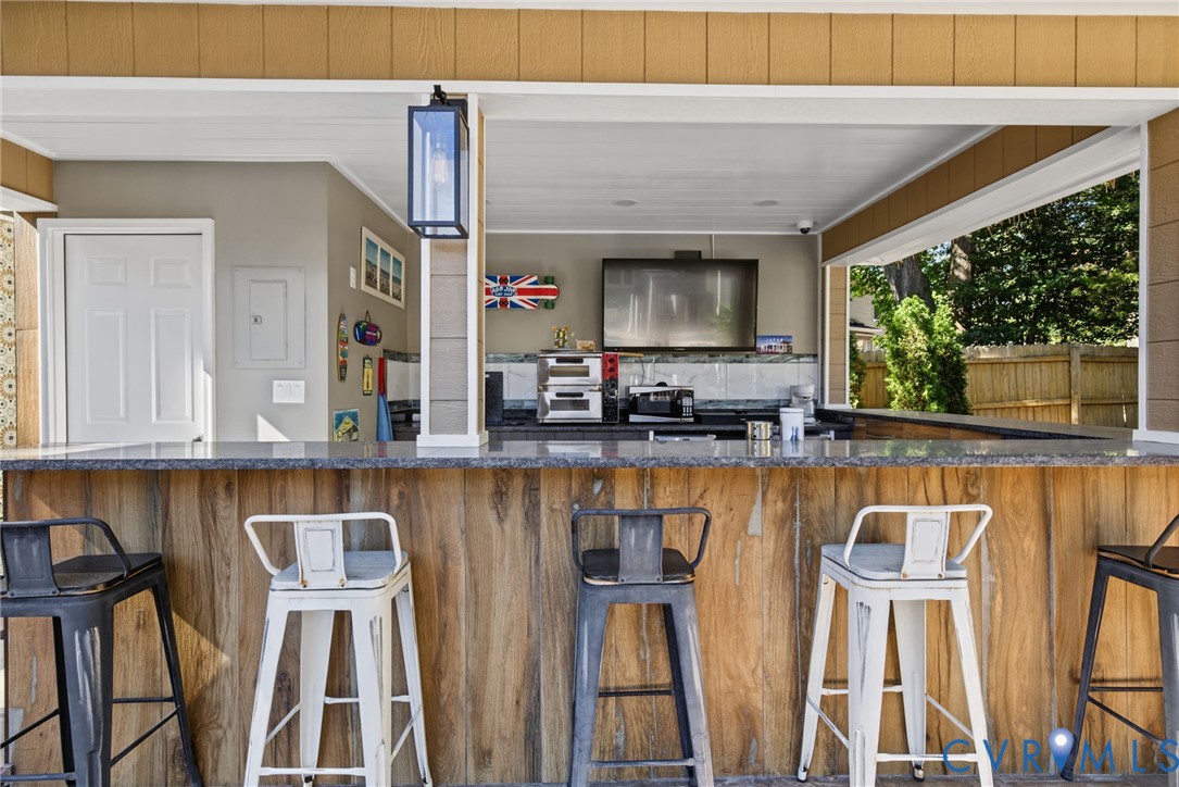 Covered outdoor kitchen featuring a stone-topped bar counter, wood-finish paneling, and an integrated exterior lantern-style lighting fixture