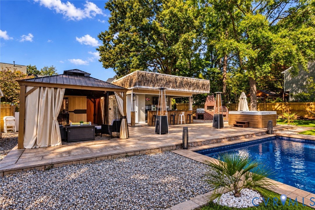*digitally enhanced to remove pool cover* Outdoor oasis featuring a paved stone patio, covered metal-roof gazebo, built-in outdoor kitchen, custom masonry fireplace, and in-ground swimming pool