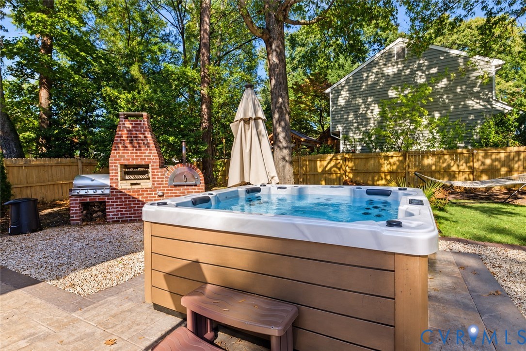 *digitally enhanced to remove spa cover* Outdoor living space featuring a built-in red brick wood-fired oven and grill, integrated hot tub, and fenced backyard area