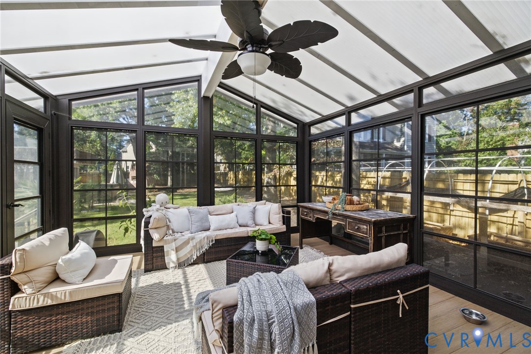 Sunroom featuring a translucent gabled roof, dark-framed multi-pane windows, wood-finish flooring, and a ceiling fan with integrated lighting