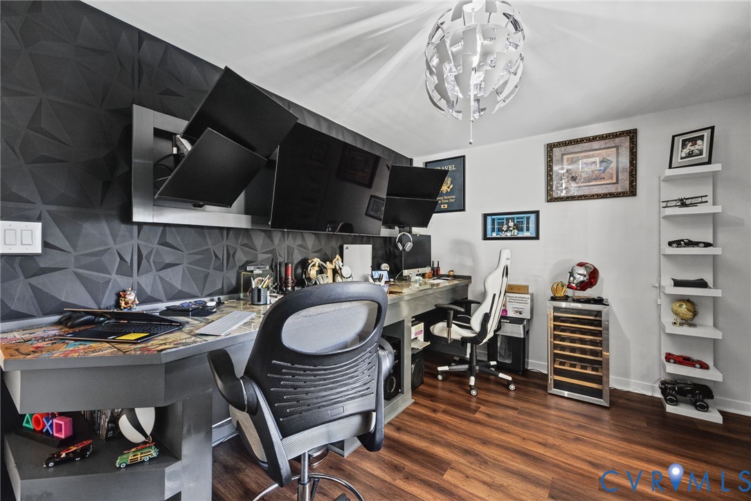 Textured geometric accent wall, built-in desk with metallic finish, wood-finish flooring, floating wall shelves, and multi-faceted modern ceiling fixture