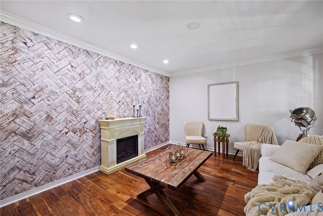 Herringbone-patterned accent wall, wood-finish flooring, built-in fireplace with a decorative mantel, and recessed lighting