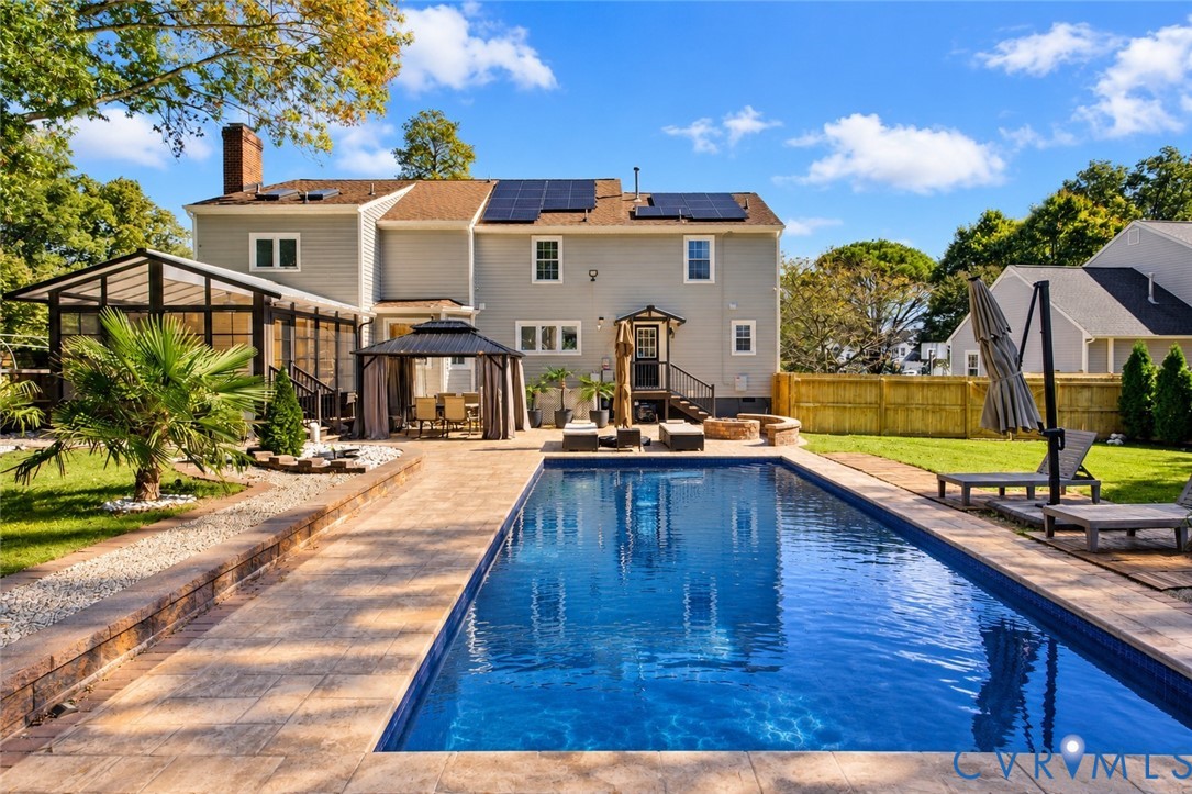 *digitally enhanced to remove pool cover* Rear exterior featuring an in-ground swimming pool, stone-paver patio, enclosed sunroom, integrated solar panels, and wood fencing