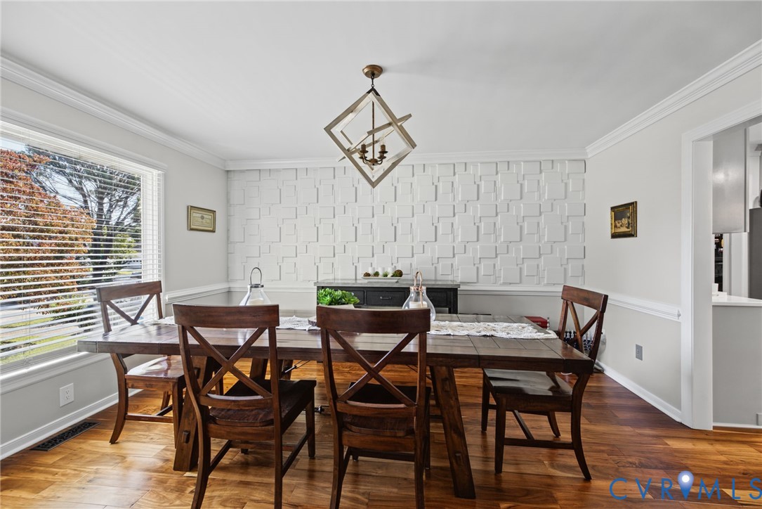 Geometric textured accent wall, wood-finish flooring, crown molding, and a contemporary multi-light metal geometric chandelier
