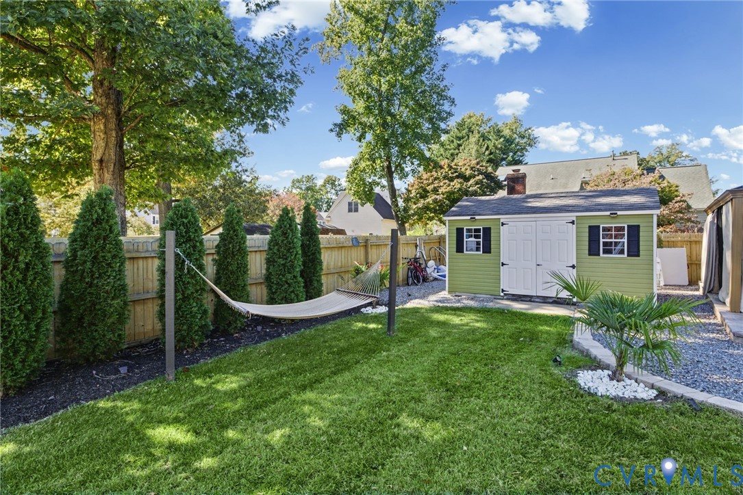 Fenced backyard featuring a manicured lawn, perimeter landscaping, stone border, and a detached storage shed