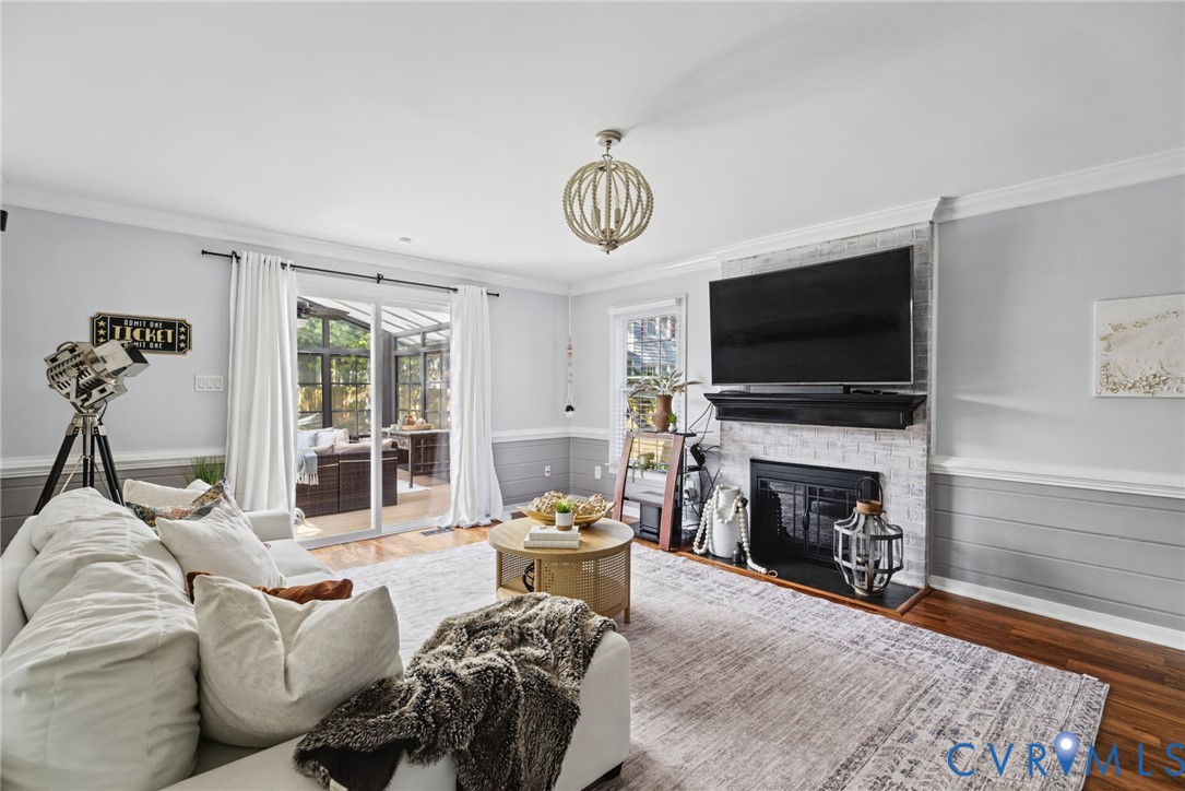 Fireplace with a whitewashed brick surround, wood-finish flooring, horizontal shiplap wall paneling, and a geometric chandelier