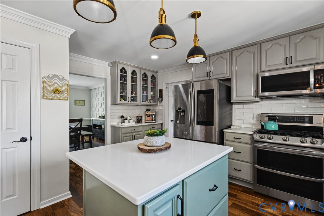 Kitchen featuring custom cabinetry, a central island with a solid surface countertop, white subway tile backsplash, stainless steel appliances, and pendant lighting