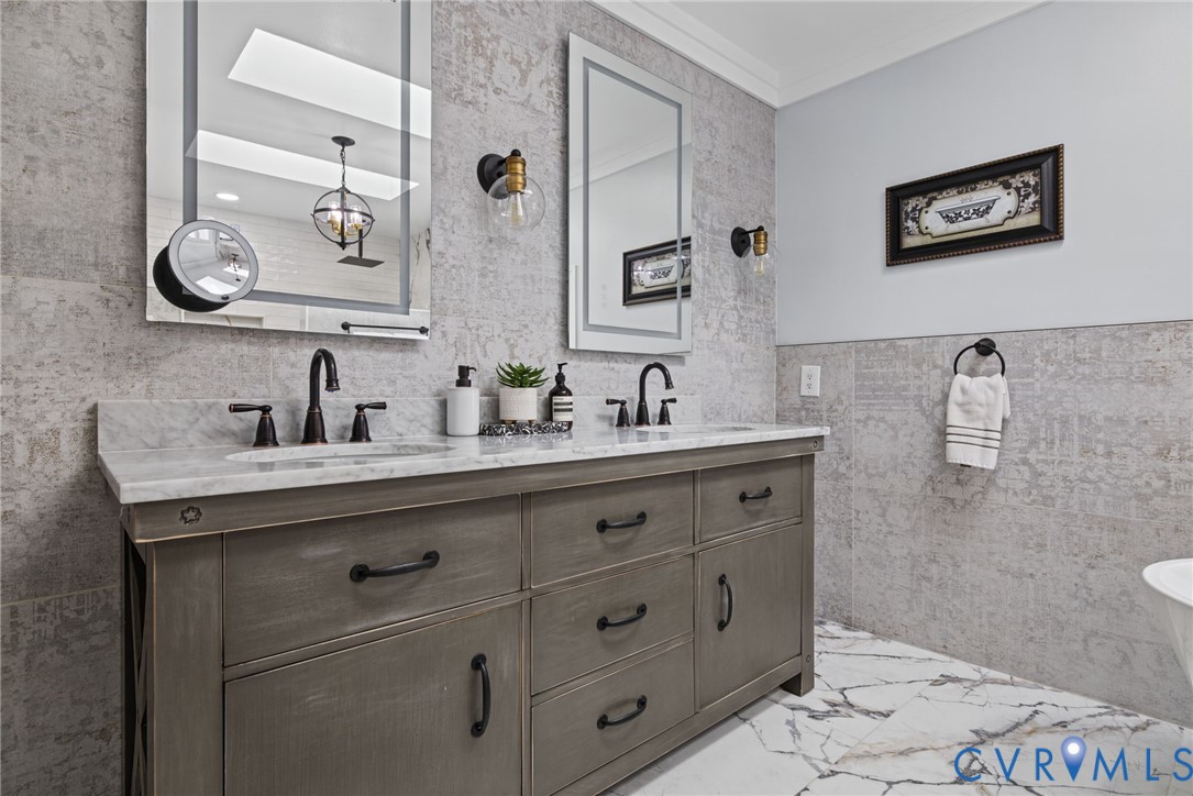 Double vanity featuring grey-tone cabinetry, stone countertop with dual undermount sinks, wall-mounted globe lighting, and matte black fixtures