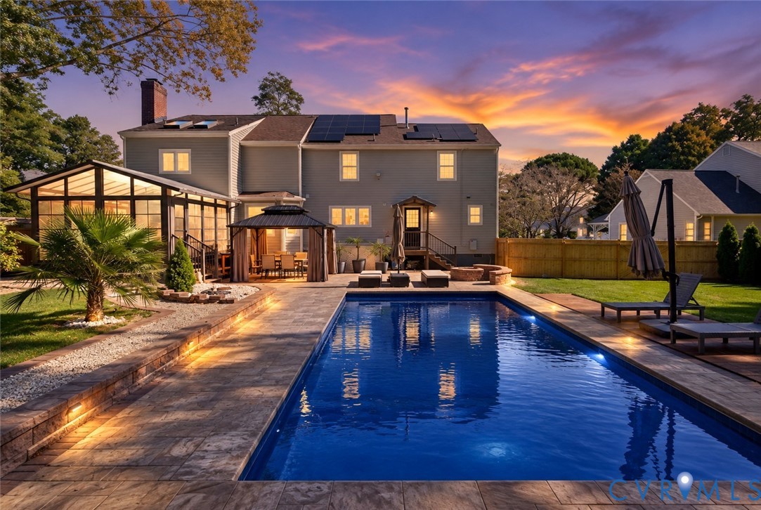 *digitally enhanced to remove pool cover* Rear exterior featuring an in-ground swimming pool, stone-paver patio, enclosed sunroom, integrated solar panels, and wood fencing