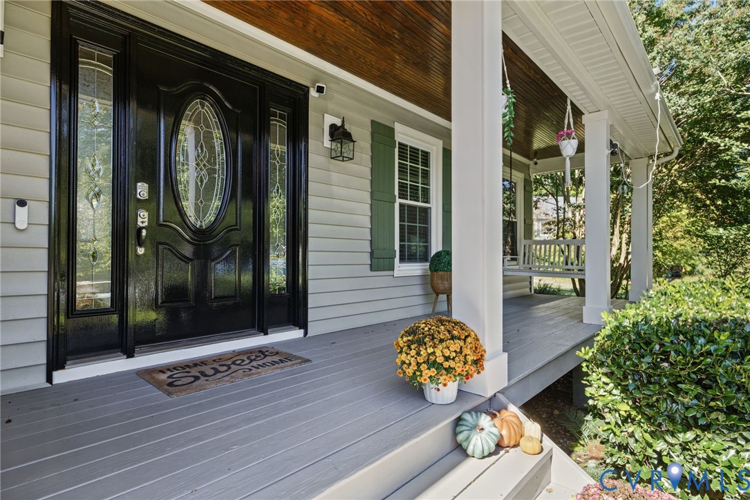 Covered front porch featuring wood-plank ceiling, structural columns, lap siding, green shutters, and a front entry door with glass sidelights and oval window detailing