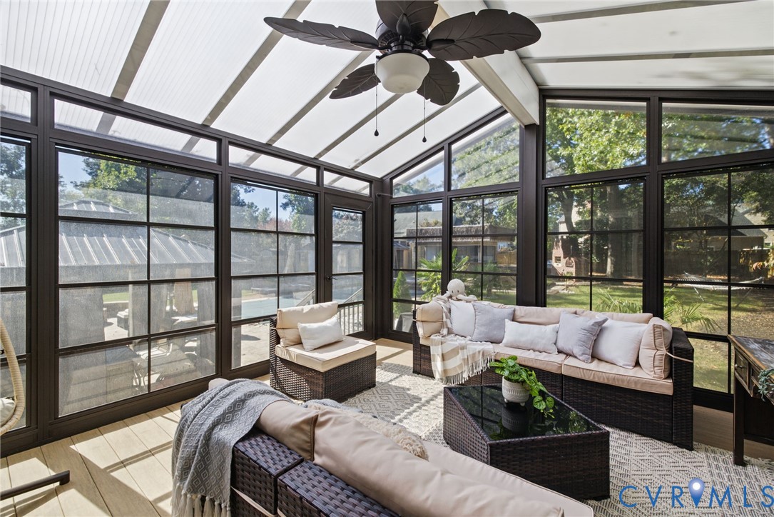 Sunroom featuring a vaulted semi-translucent roof, dark-framed grid windows, wood-finish flooring, and a ceiling fan with leaf-motif blades