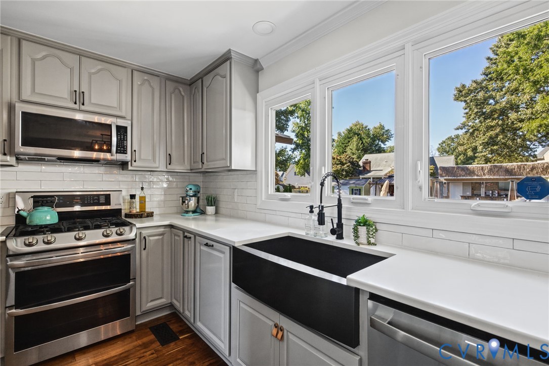 Kitchen featuring soft-gray cabinetry, quartz countertops, white subway tile backsplash, stainless steel gas range with microwave, and a black apron-front sink with a matte black faucet
