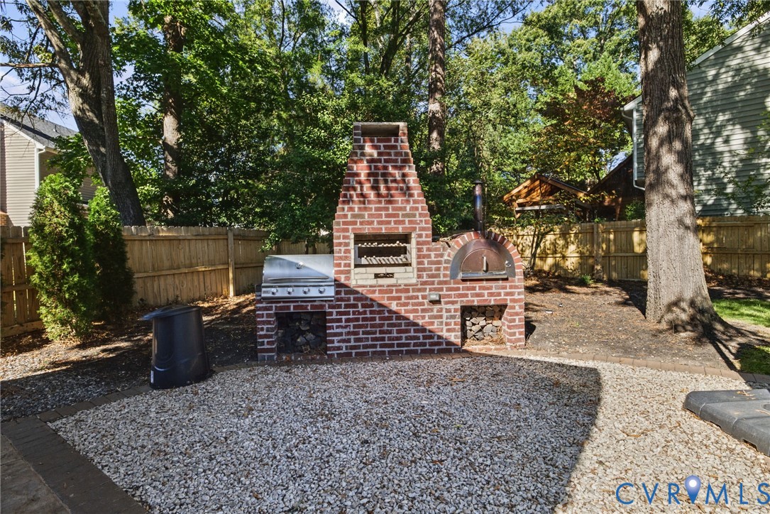 Outdoor masonry structure featuring a brick fireplace, built-in stainless steel grill, integrated pizza oven, and dual wood storage niches set upon a stone-surfaced patio