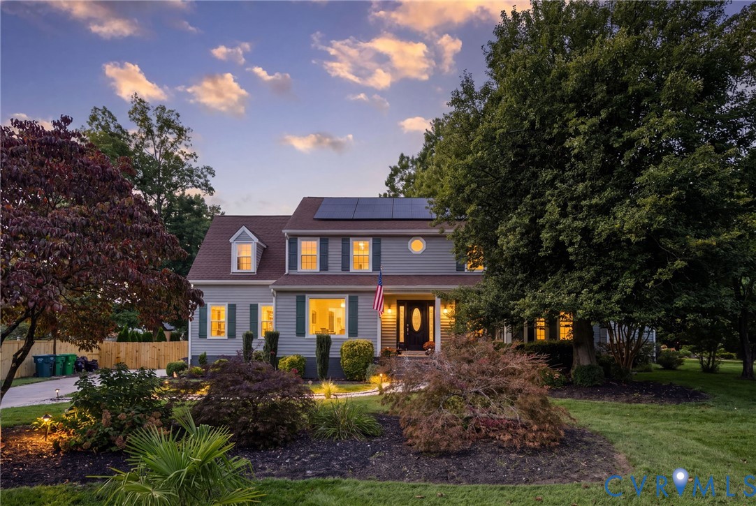 * Digitally altered to simulate twilight* Two-story residence featuring grey lap siding, rooftop solar panels, dark-toned shutters, a prominent roof dormer, and a covered front entryway with a decorative glass-panel door * Digitally altered to simulate twilight* Two-story residence featuring grey lap siding, rooftop solar panels, dark-toned shutters, a prominent roof dormer, and a covered front entryway with a decorative glass-panel door