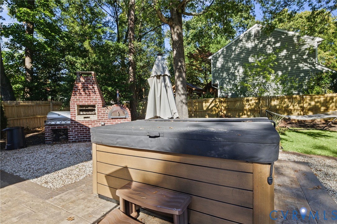 Outdoor space featuring a built-in brick fireplace and pizza oven, integrated spa, and stamped concrete patio surfacing