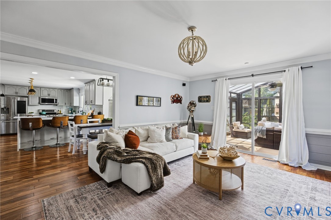 Open-concept interior featuring wood-finish flooring, crown molding, chair rail trim, a multi-light spherical chandelier, and sliding glass doors