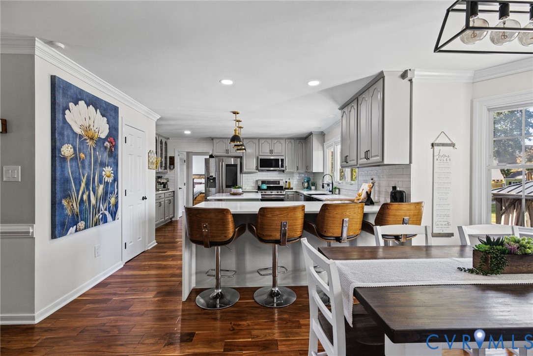 Kitchen featuring wood-finish flooring, white cabinetry, quartz-surface breakfast bar, recessed lighting, and stainless steel appliances