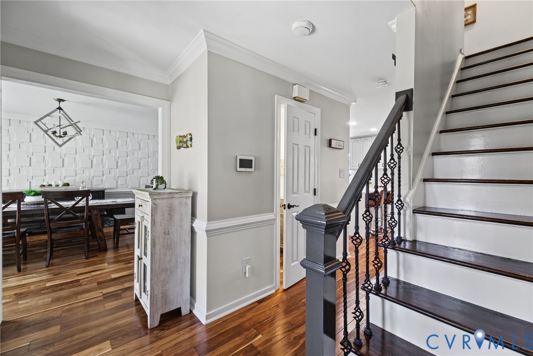 Foyer featuring wood-finish flooring, staircase with dark-finished wood treads and metal balusters, crown molding, and wainscoting