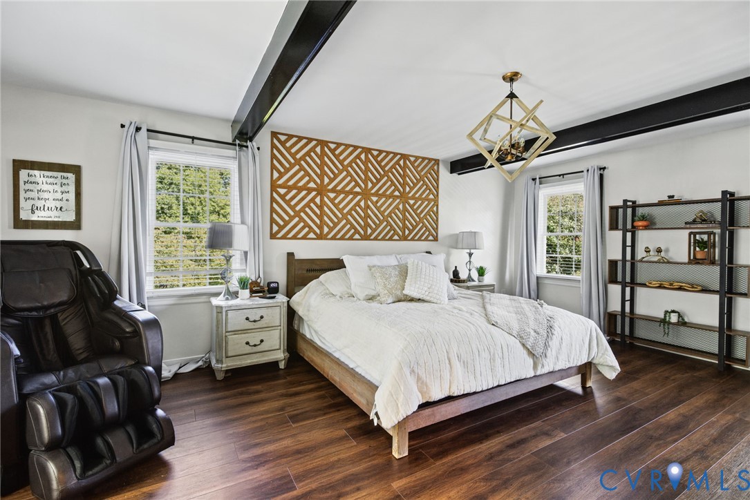 Bedroom featuring wood-finish flooring, exposed black ceiling beams, geometric wall accent paneling, and a metallic geometric pendant light fixture