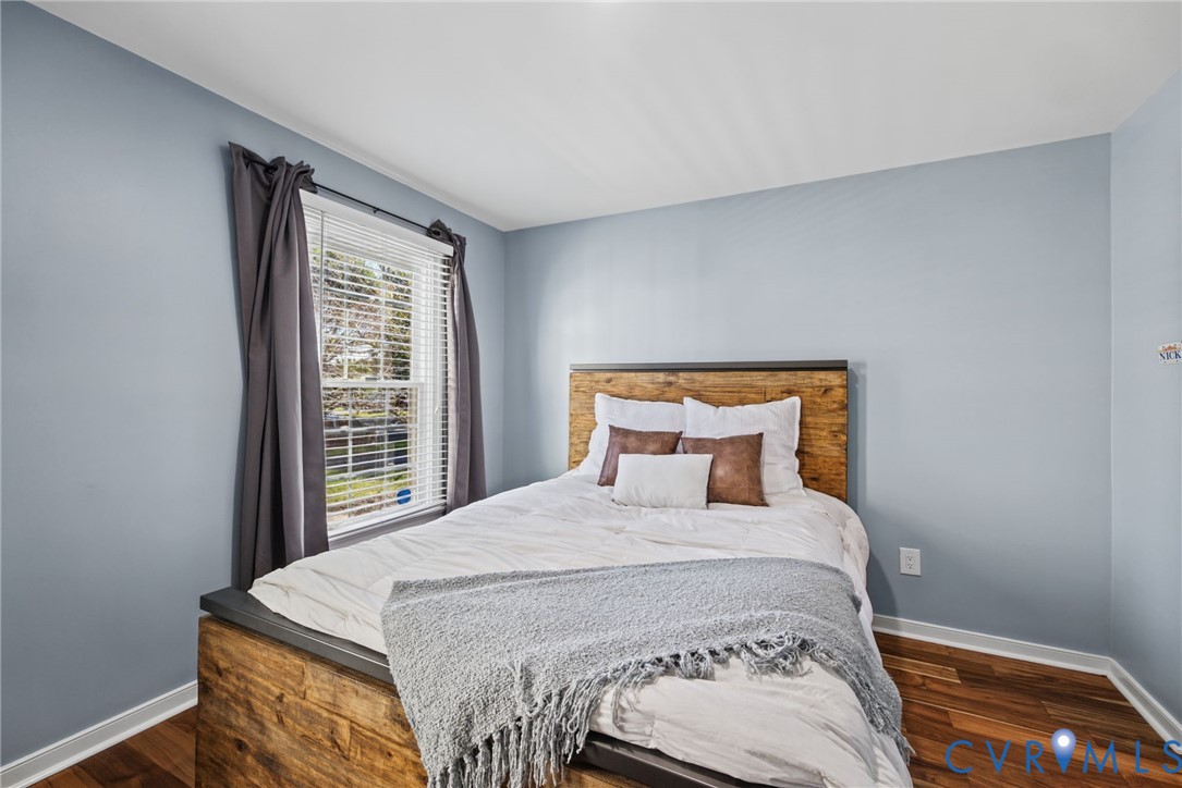 Room featuring wood-finish flooring, light blue wall paint, and a single-pane window with horizontal blinds