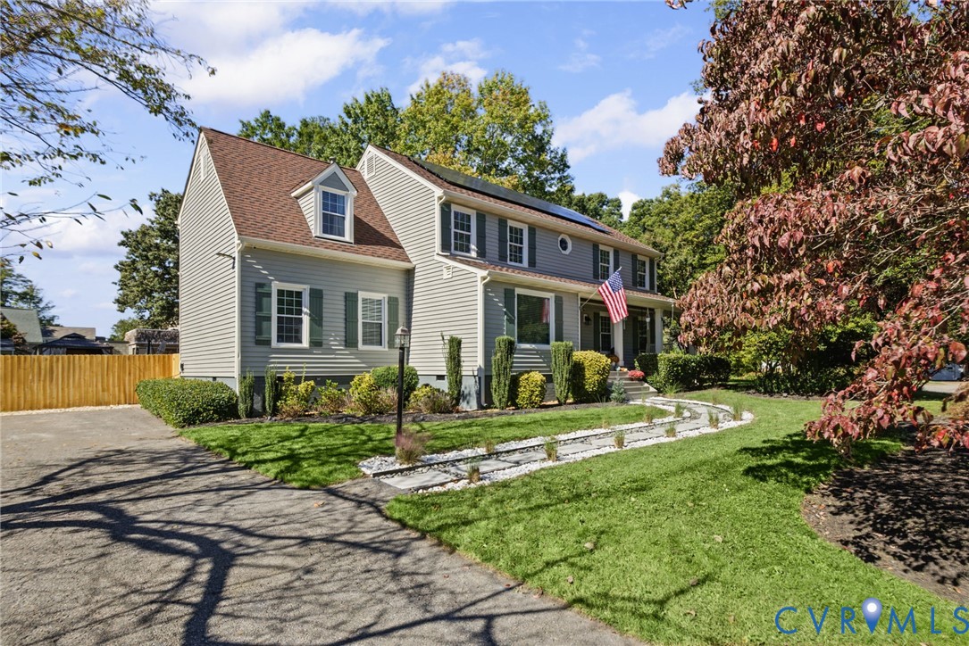 Two-story residence featuring light gray siding, a shingled roof with integrated solar panels, a stone-lined walkway, and landscaped garden beds