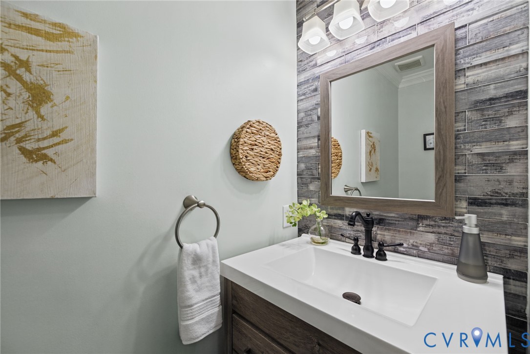 Vanity featuring a white countertop, undermount sink, dark-finish widespread faucet, and wood-finish cabinetry, accented by horizontal tile wall cladding, a framed mirror, and a multi-bulb light fixture