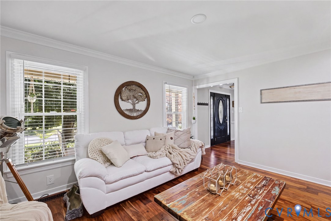 Living area featuring wood-finish flooring, recessed lighting, crown molding, and dual windows with plantation-style shutters