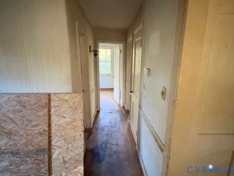 Hallway featuring wood-finish flooring, wainscoting, and a wall-mounted light fixture