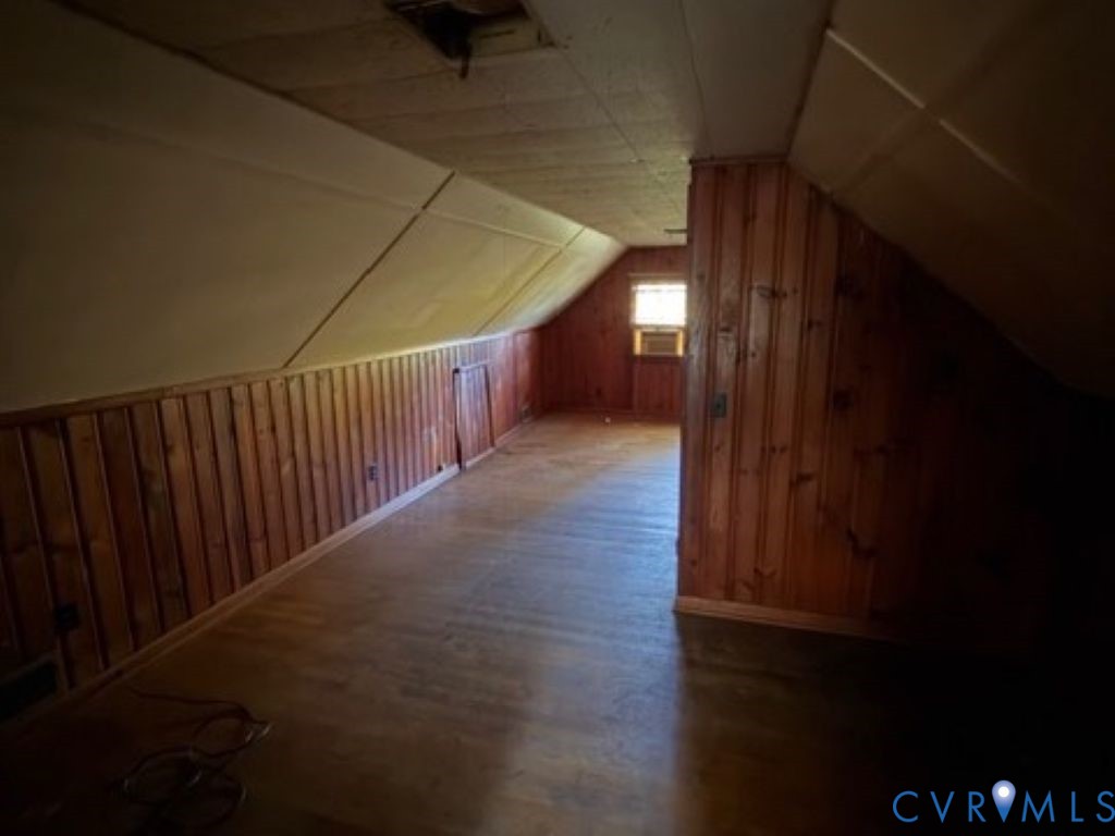 Finished attic space featuring wood-panelled walls, slanted ceilings, and wood-finish flooring