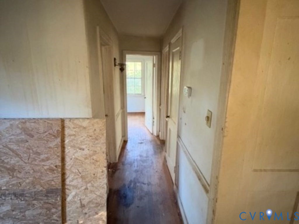 Hallway featuring wood-finish flooring, wainscoting, and a wall-mounted sconce
