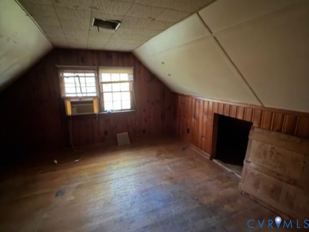 Attic space featuring wood-finish wall paneling, sloped ceilings, multi-pane windows, and wood-finish flooring
