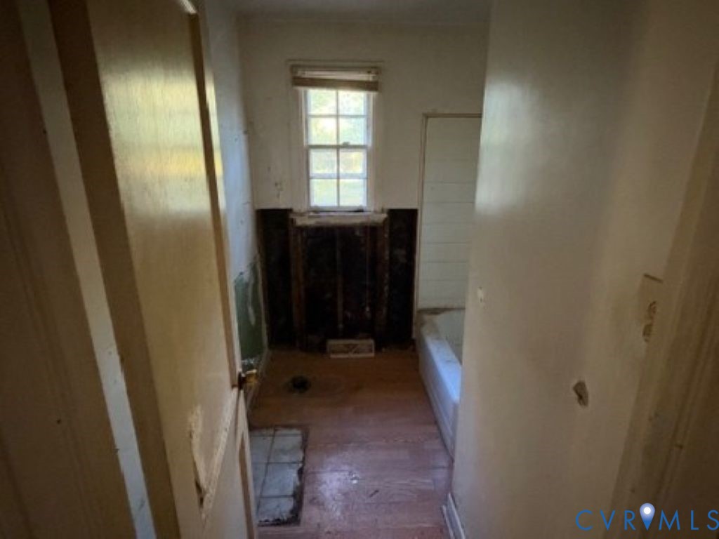Single-pane sash window with integrated muntins, wood-finish flooring, and a standard-size bathtub enclosure