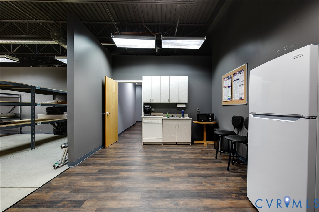 Kitchenette featuring cabinetry, an integrated sink, and dishwasher, wood-finish flooring, and an exposed ceiling structure