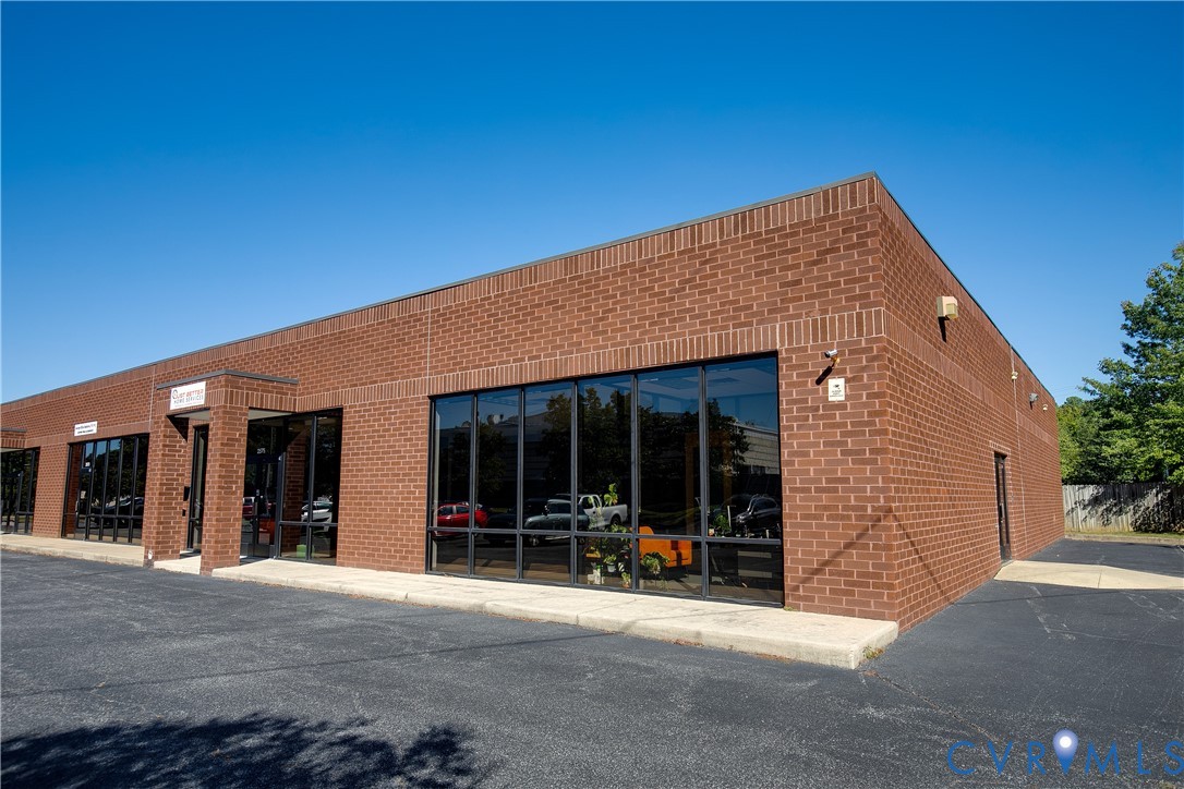 Commercial exterior featuring a red brick facade, floor-to-ceiling glass paneling, and an asphalt parking surface