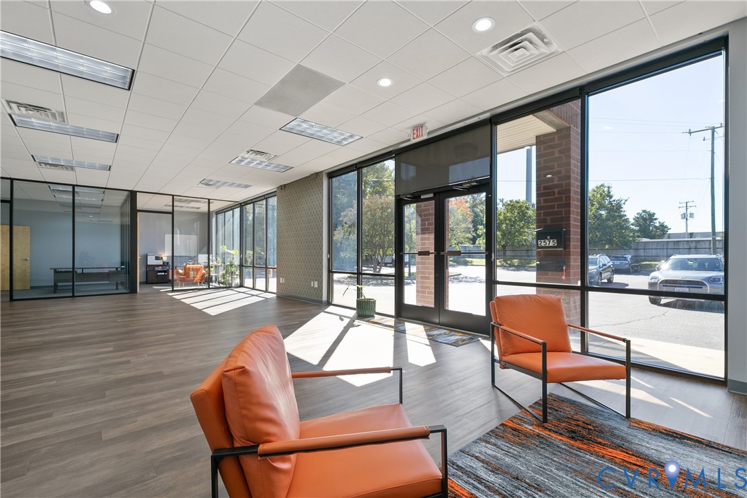 Expansive commercial interior featuring floor-to-ceiling glass panel walls, wood-finish flooring, recessed lighting, and a glass-paneled entry door with brick masonry detailing
