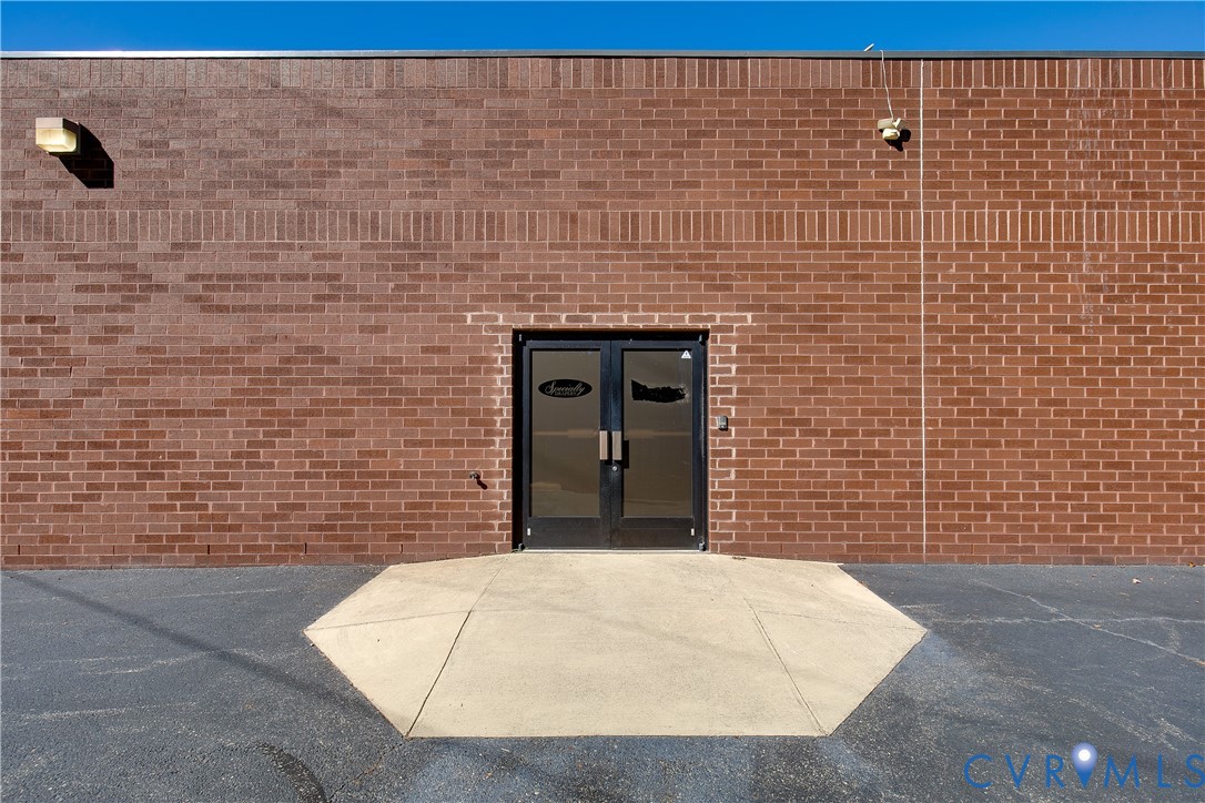 Exterior facade featuring a durable brick masonry wall, double glass entry doors with aluminum frames, and a concrete landing pad