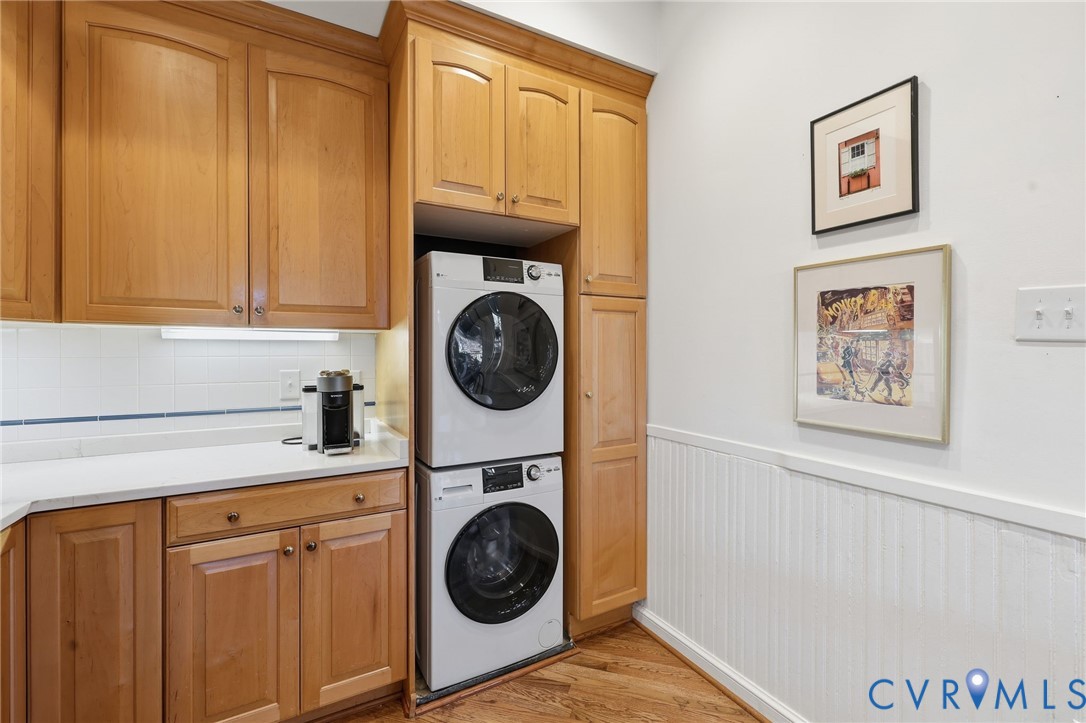 Laundry area featuring light-finish cabinetry, solid-surface countertops, beadboard wainscoting, and wood-finish flooring