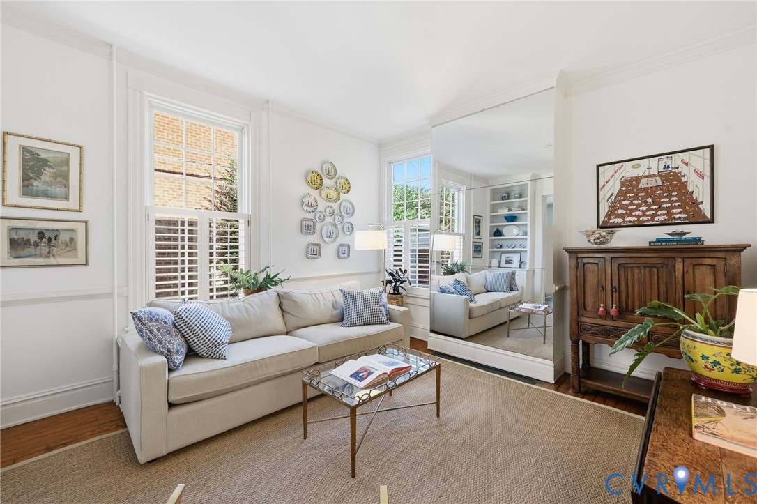 Living area featuring tall windows with interior shutters, wall-to-wall mirror paneling, built-in shelving, and wood-finish flooring
