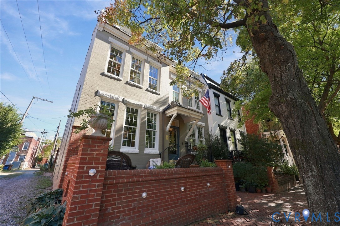 Three-story brick exterior featuring a prominent red brick perimeter wall, multi-pane windows, a covered entryway with decorative bracket supports, and a brick-paved front landing