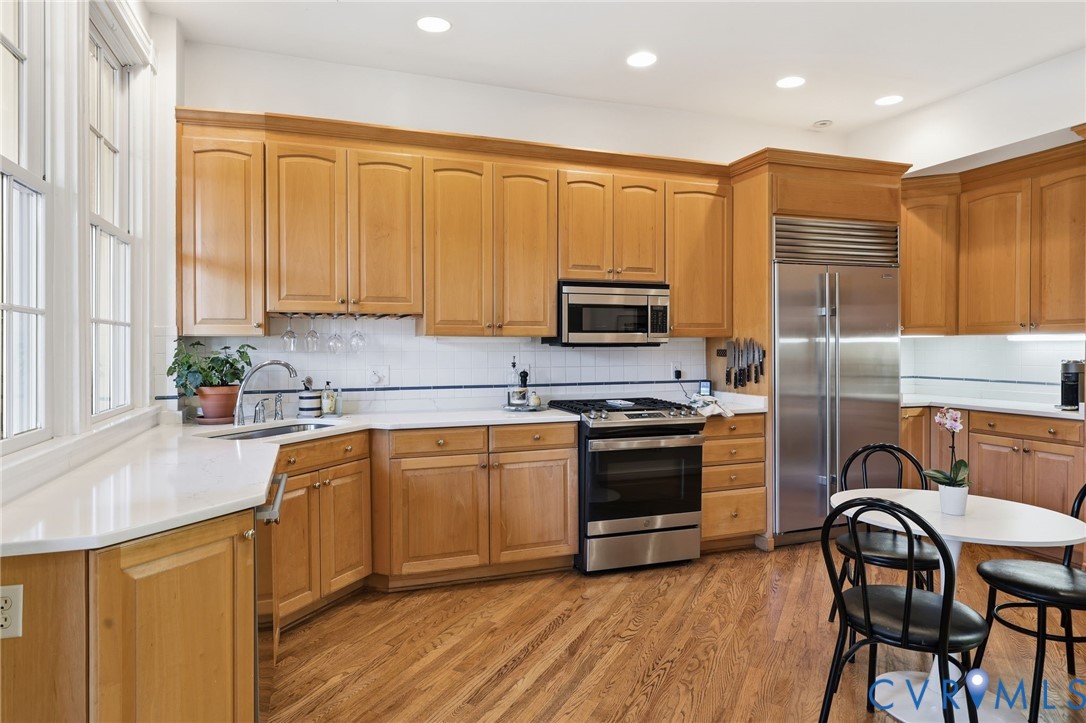Kitchen featuring custom wood cabinetry, stainless steel professional-grade refrigerator, gas range, recessed lighting, and wood-finish flooring