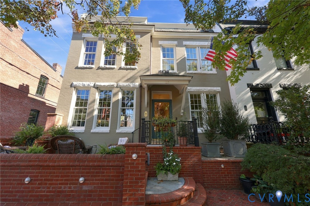 Painted brick exterior featuring a covered entryway, multi-pane windows with stone-style lintels, and a low-profile red brick retaining wall with integrated lighting Painted brick exterior featuring a covered entryway, multi-pane windows with stone-style lintels, and a low-profile red brick retaining wall with integrated lighting
