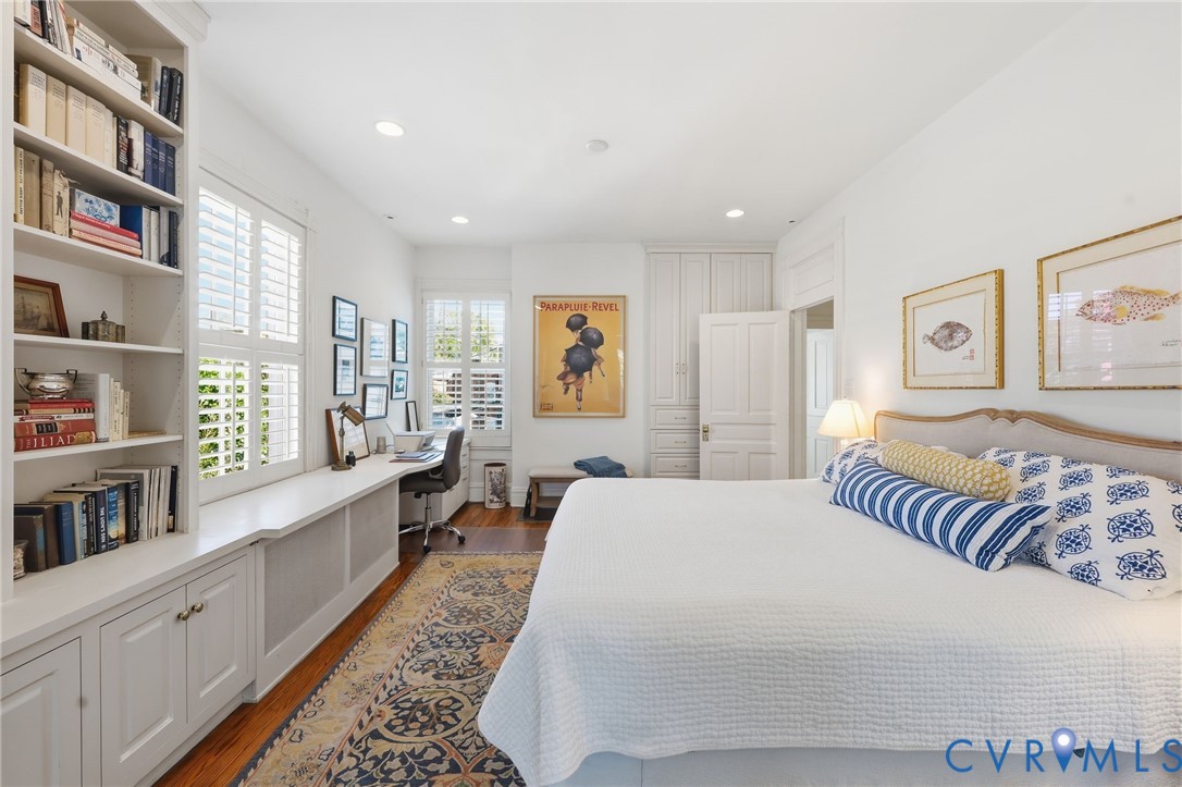 Custom built-in cabinetry featuring floor-to-ceiling bookshelves, integrated desk space, recessed ceiling lighting, plantation shutters, and wood-finish flooring