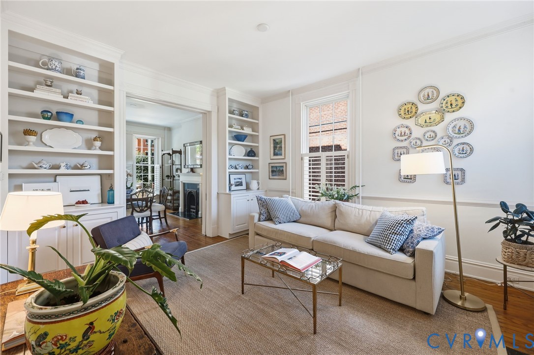 Living area featuring tall built-in bookshelves, chair rail molding, wood-finish flooring, and multi-pane windows with interior shutters Living area featuring tall built-in bookshelves, chair rail molding, wood-finish flooring, and multi-pane windows with interior shutters