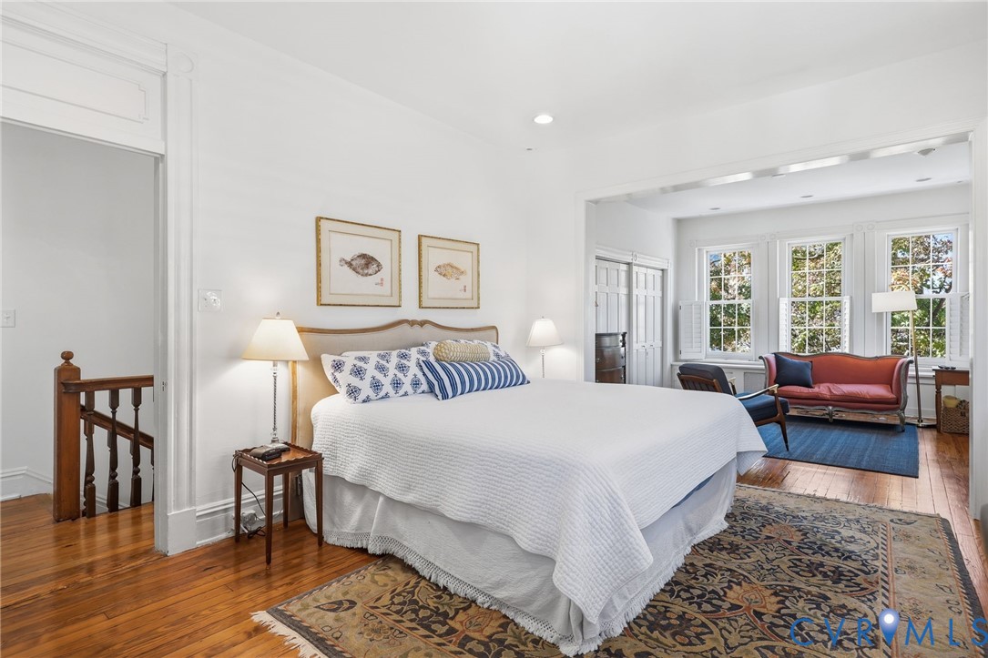 High-ceiling interior featuring wood-finish flooring, multi-pane windows with plantation shutters, recessed lighting, and white-painted trim