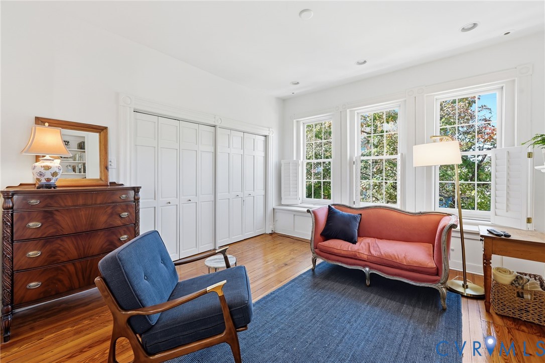 Wood-finish flooring, multi-panel sliding closet doors, recessed lighting, and large windows with interior shutters