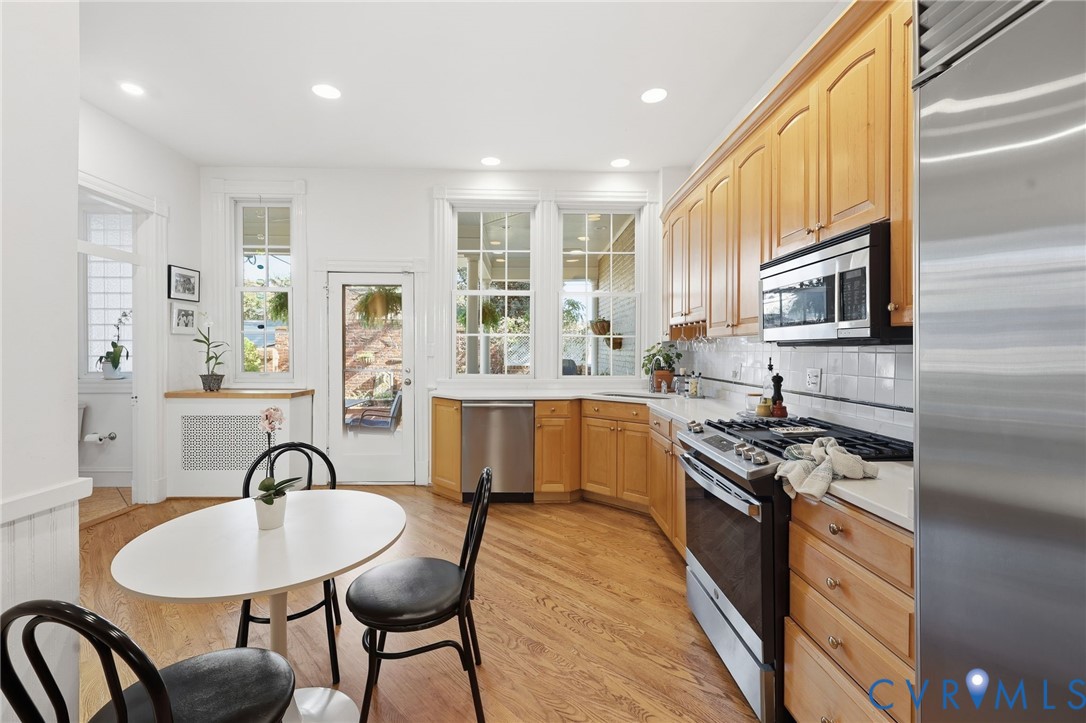 Kitchen featuring recessed lighting, wood cabinetry, stainless steel appliances, white tile backsplash, and wood-finish flooring