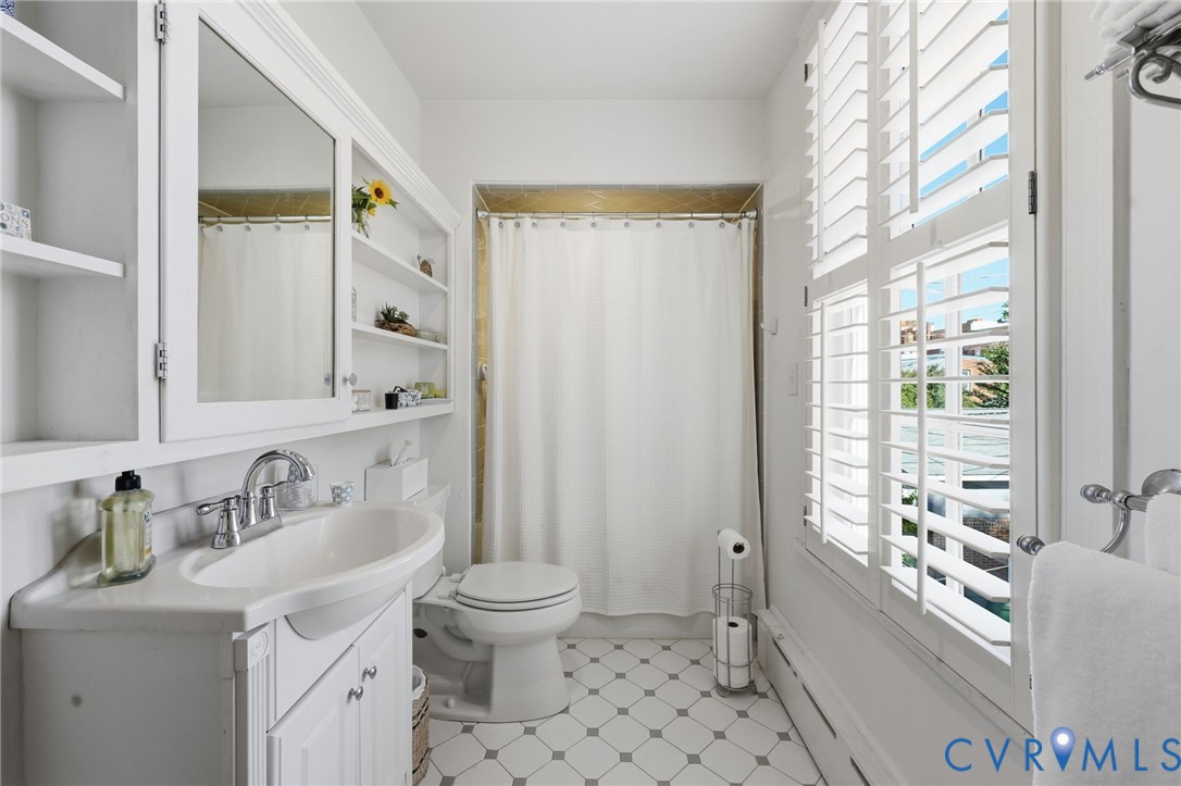 Bathroom featuring a pedestal-style vanity with integrated sink, built-in recessed shelving, plantation shutters, and geometric patterned floor tile