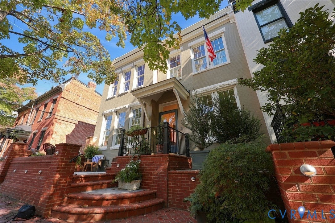 Painted brick exterior featuring a prominent covered entry portico, tiered brick masonry steps, and custom black metal railings